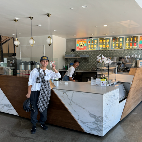 Bright and modern interior of Bicycle Coffee’s Breuner Building cafe in Oakland, featuring geometric marble and wood counters, smiling baristas, and colorful drink menu boards