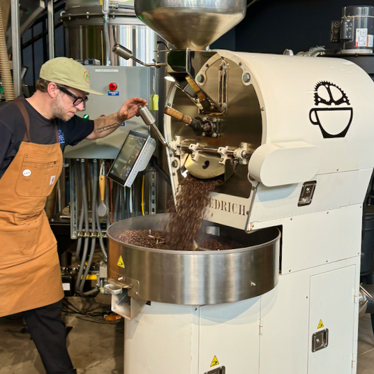Bicycle Coffee roaster operating a Diedrich roasting machine as freshly roasted coffee beans drop into the cooling tray.